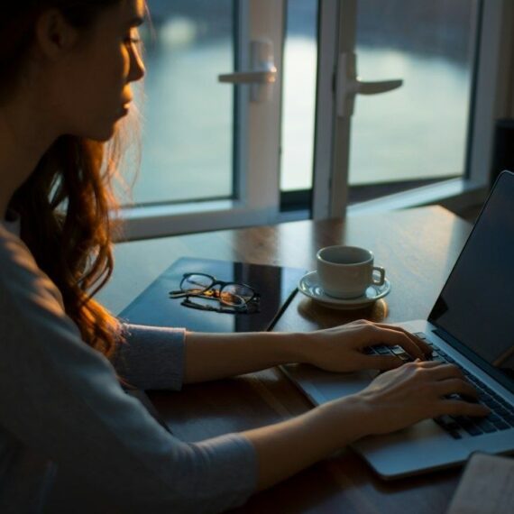 Person arbejder ved en bærbar computer med en kaffekop ved siden af