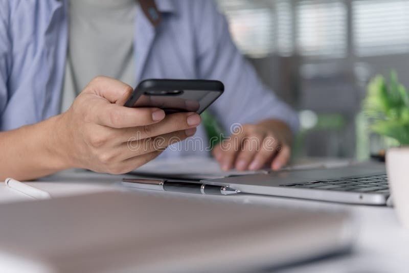 Person holder en smartphone ved siden af en bærbar computer på et skrivebord